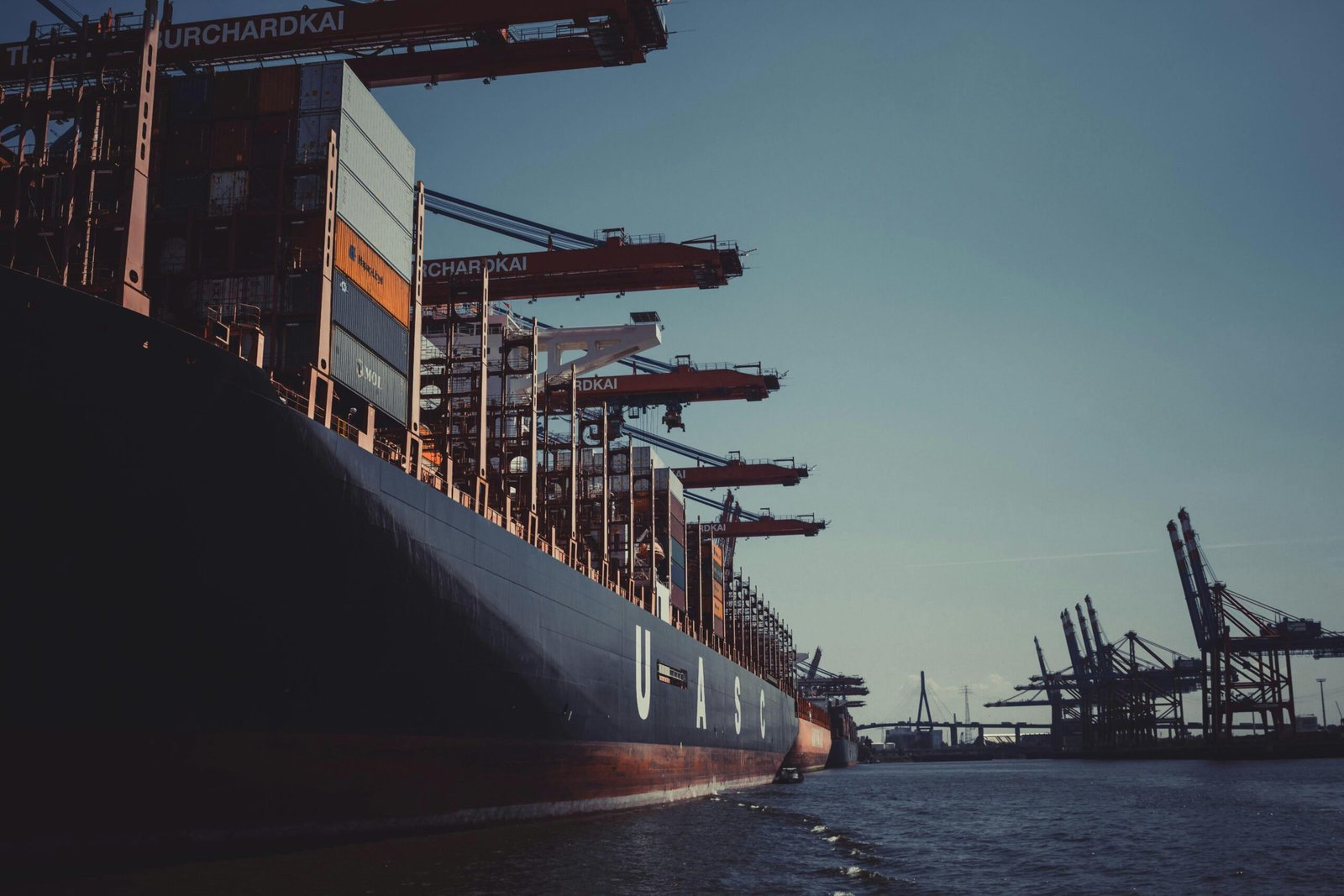 Large cargo ship loaded with containers at a port with cranes, representing international shipping and logistics operations