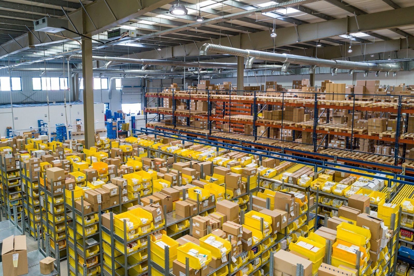 Large industrial warehouse with organized shelves, stacked packages, and yellow storage bins used for logistics, inventory management, and order fulfillment.